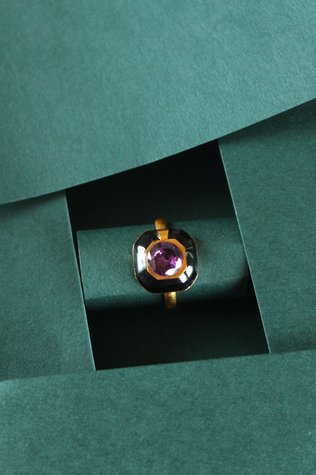 Gold bezel ring surrounded by a square black enamal frame with a round white stone ring
